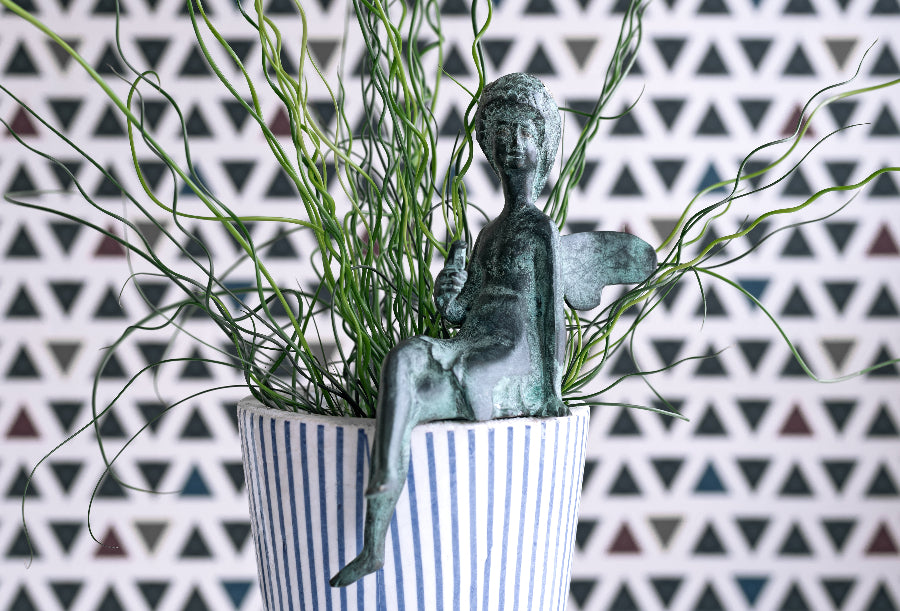 Statue of a child in a striped pot with greenery against a geometric patterned wall.