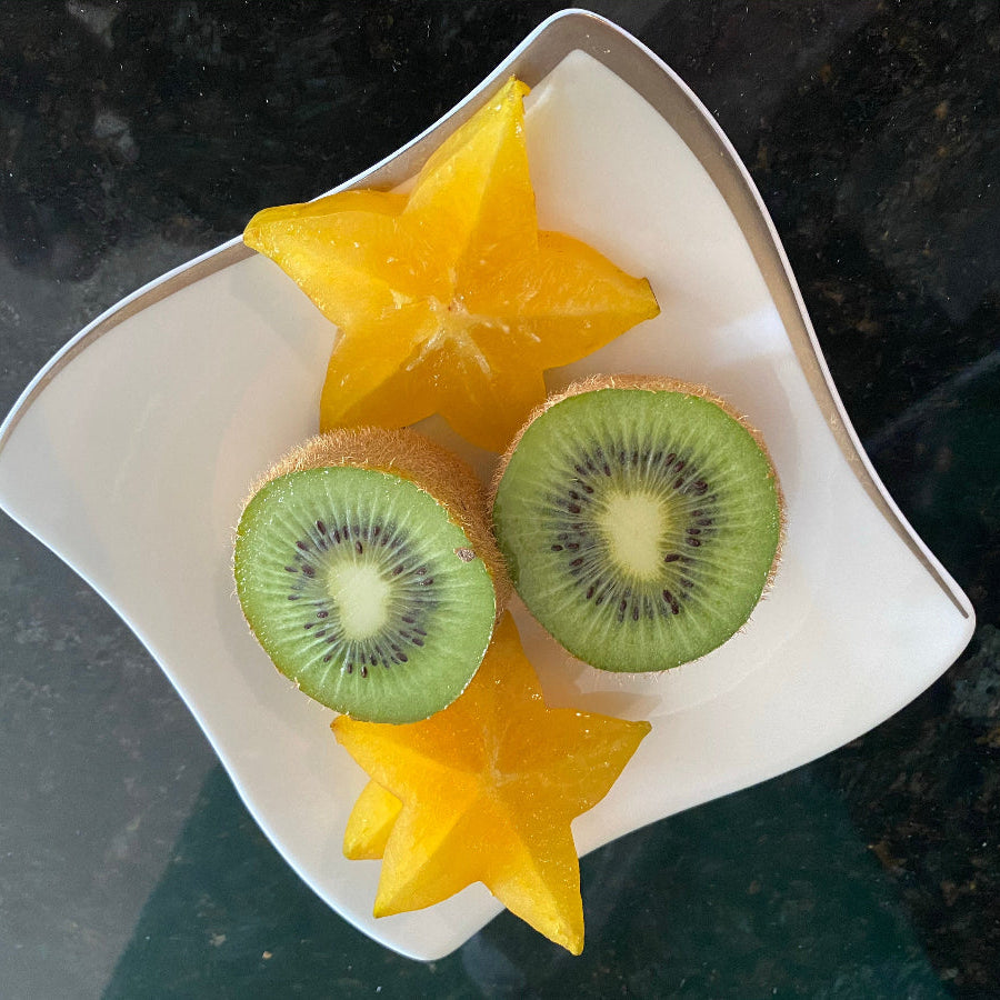Sliced yellow star fruit and green kiwi served on a white plate